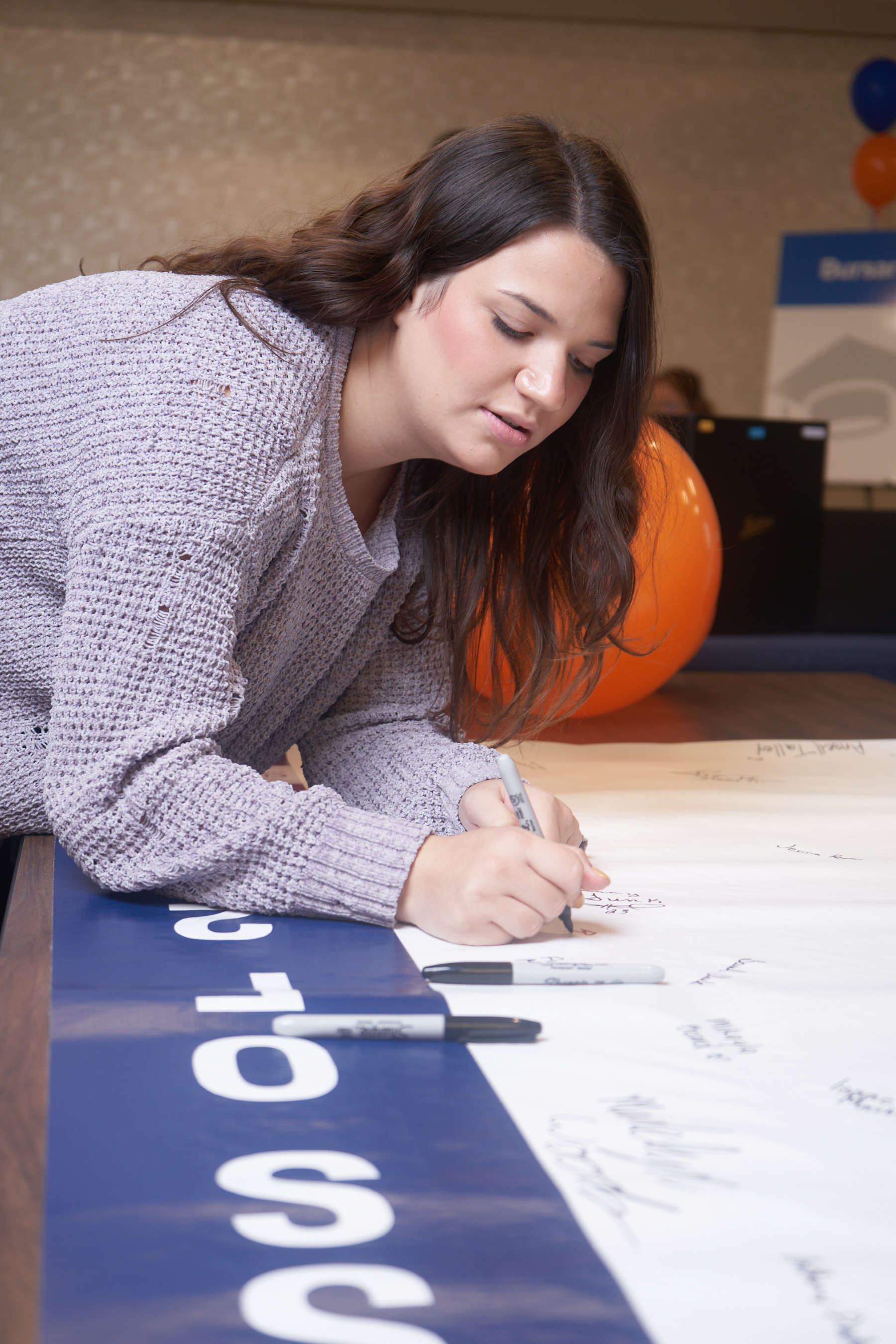 Rachel B., a university transfer student, signs a banner for graduates.