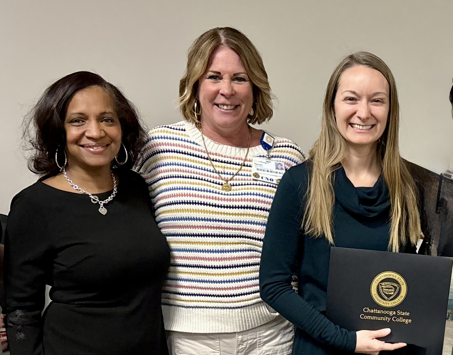 Three women stand side by side with one holding a certificate.