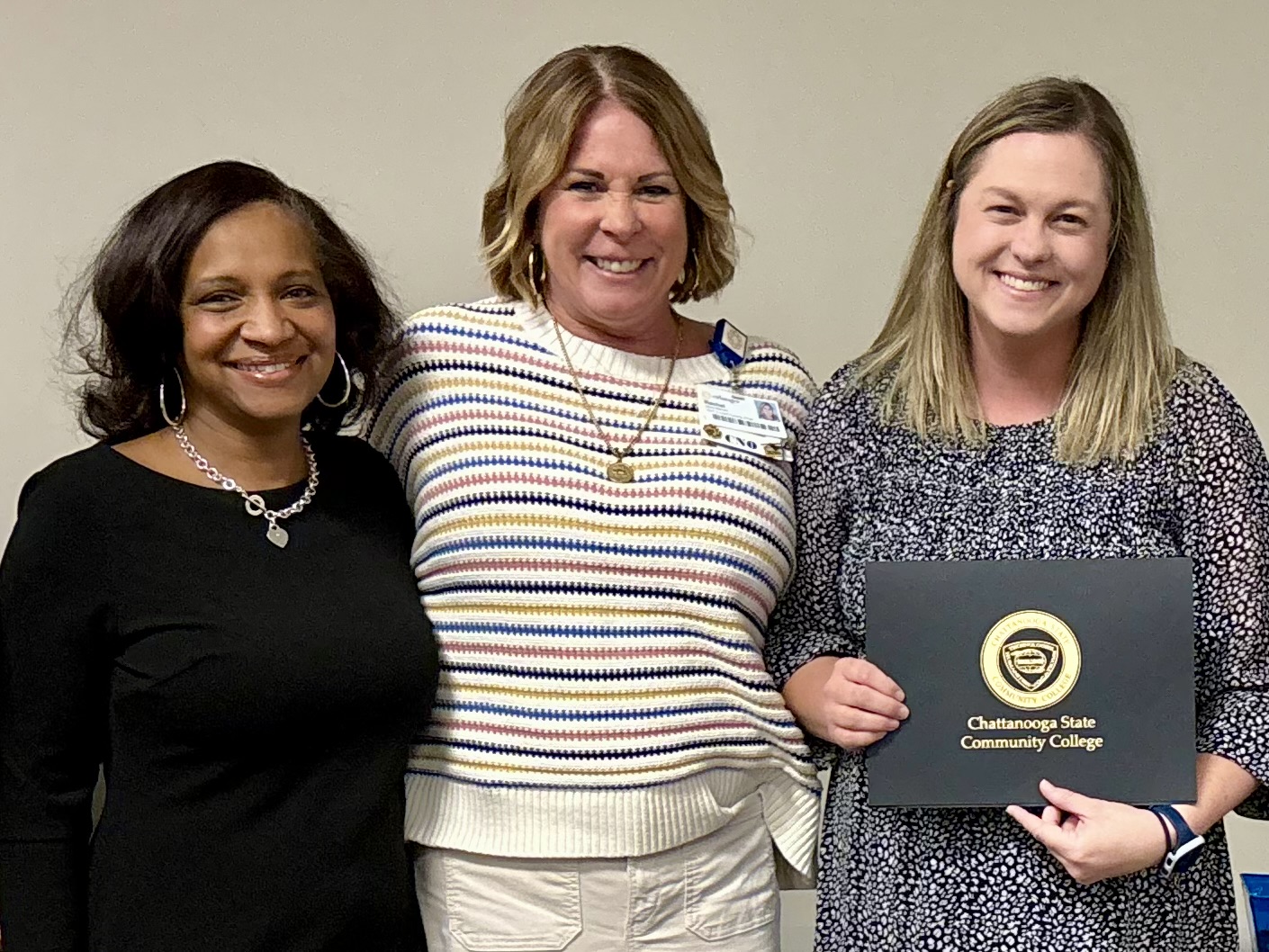 Three women stand side by side with one holding a certificate.