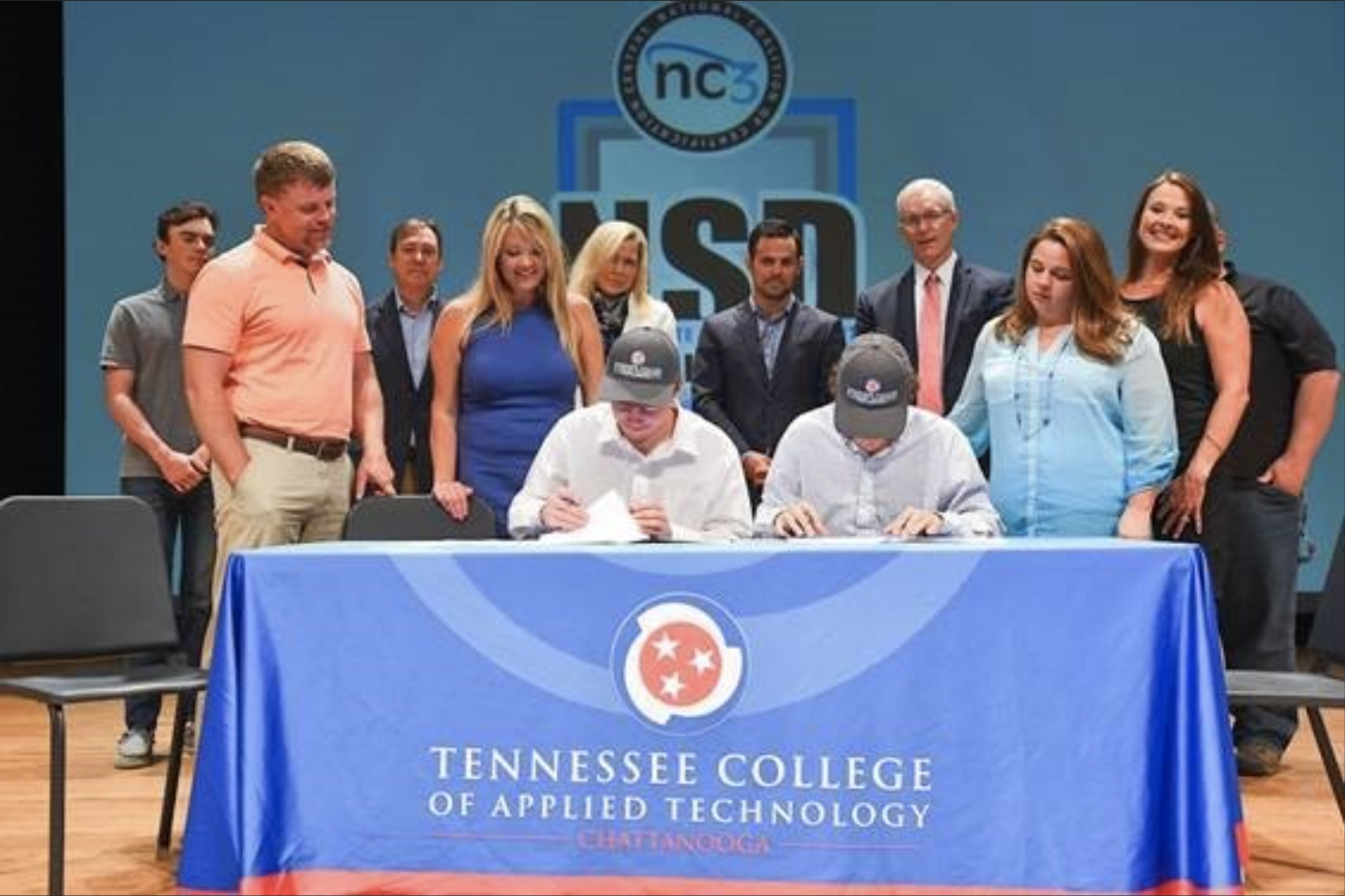 two students seated at a table draped in a blue tablecloth with the TCAT logo emblazoned upon it