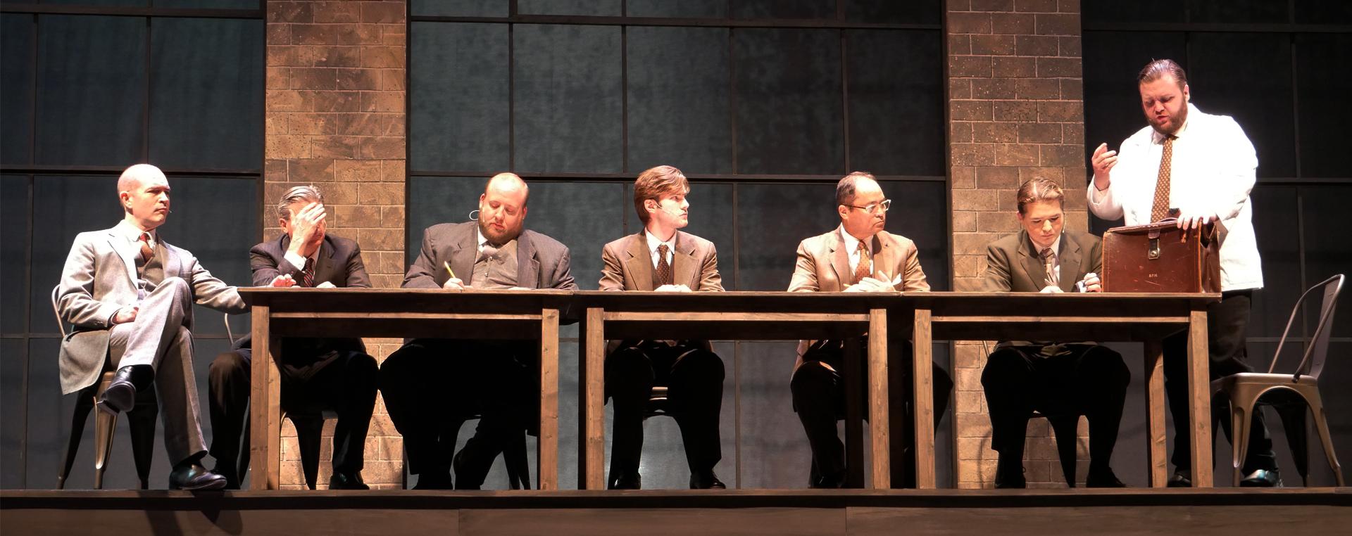 men sitting at a table on stage looking serious
