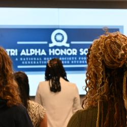 Women in focus look on at an out-of-focus sign that reads "Tri-Alpha Honor Society"