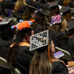 A woman sititng in a crowd of graduates wears a decorated mortaboard that reads "Class of 2025" A woman sititng in a crowd of graduates wears a decorated mortaboard that reads "Class of 2025"