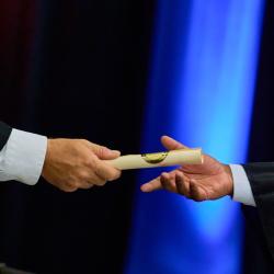 A close up of one person handing a diploma to another person.