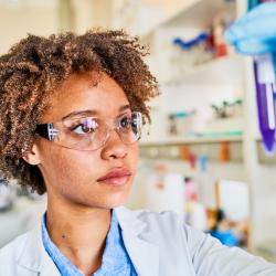A Medical Laboratory Technician in a white lab coat looks at a medical sample in a plastic tube. A Medical Laboratory Technician in a white lab coat looks at a medical sample in a plastic tube.