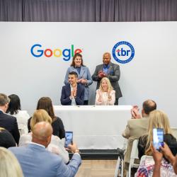 Rob Magliaro and Flora Tidings sit in front of a Google and TBR sign while onlookers cheer.