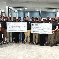 A group of well-dressed students, faculty, and business leaders hold two oversized checks from TVA and Westinghouse.