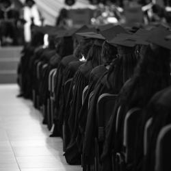 Students in graduation regalia sit in an auditorium. 