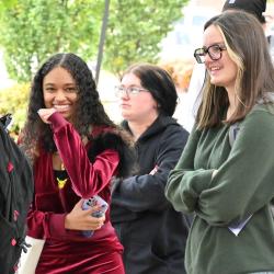 Three younger women stand in line as one smiles toward the camera.