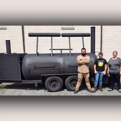 2 women and 1 man with bbq smoker they built in welding class