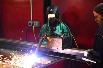 A young woman and an instructor look on at a welding machine. A young woman and an instructor look on at a welding machine.
