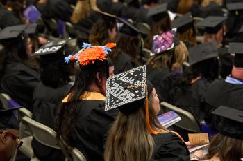 A woman sititng in a crowd of graduates wears a decorated mortaboard that reads "Class of 2025" A woman sititng in a crowd of graduates wears a decorated mortaboard that reads "Class of 2025"