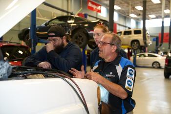 An instructor and two students look under the hood of a car. An instructor and two students look under the hood of a car.
