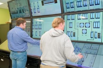 Two male students interract with an educational digital nuclear control room display.