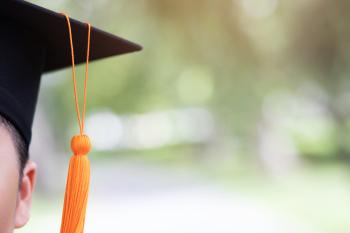 Partial view of an ambiguous student's face wearing a black mortarboard and orange tassle. Out of focus trees are visible in the background. Partial view of an ambiguous student's face wearing a black mortarboard and orange tassle. Out of focus trees are visible in the background.