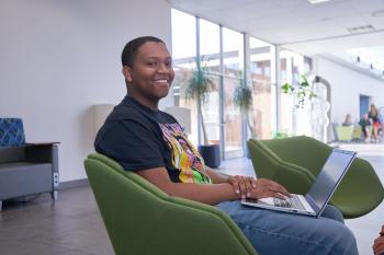 A student sits in a chair in the OMNI building at ChattState with a computer on his lap.