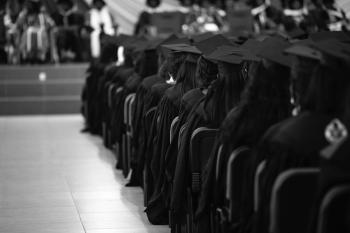 Students in graduation regalia sit in an auditorium. 