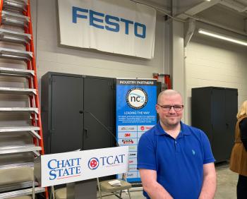 Student John Jordan stands in front of a lectern and signage for ChattState, TCAT, and industry partners.