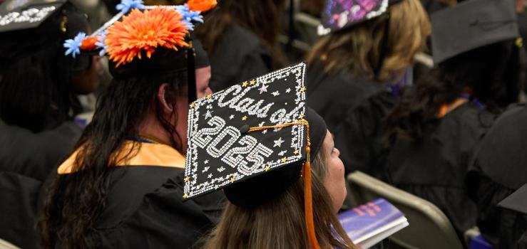A woman sititng in a crowd of graduates wears a decorated mortaboard that reads "Class of 2025"