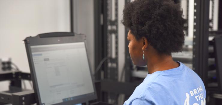 A woman in a blue shirt types on a computer.