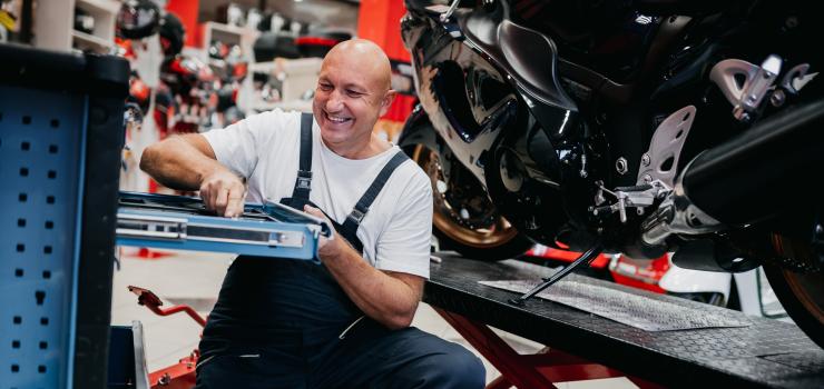 a man working in a garage, reaching into a tool box, with a motorcycle behind him